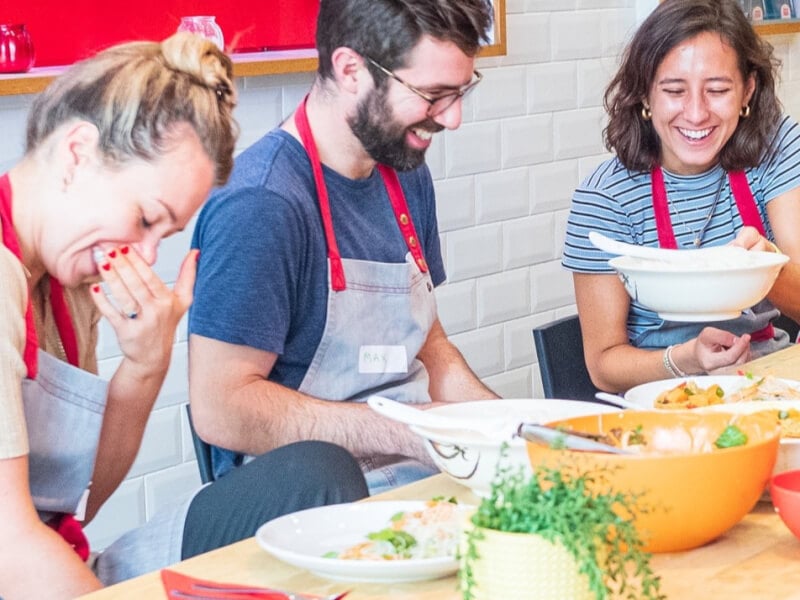 A man and two women are laughing at a School of Wok cooking class